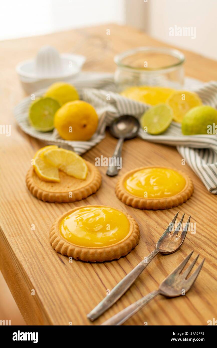 Einige frisch gebackene Plätzchen oder Kuchen mit Zitronenquark, Zutaten auf einem Holztisch wie Zitronen, Orangen, Limetten. Gabeln und Löffel gebrauchsfertig. Stockfoto