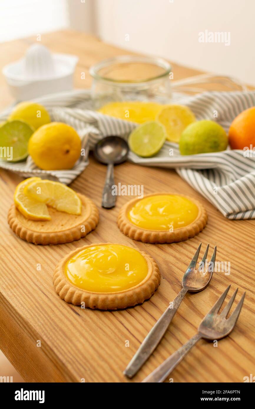 Einige frisch gebackene Plätzchen oder Kuchen mit Zitronenquark, Zutaten auf einem Holztisch wie Zitronen, Orangen, Limetten. Gabeln und Löffel gebrauchsfertig. Stockfoto