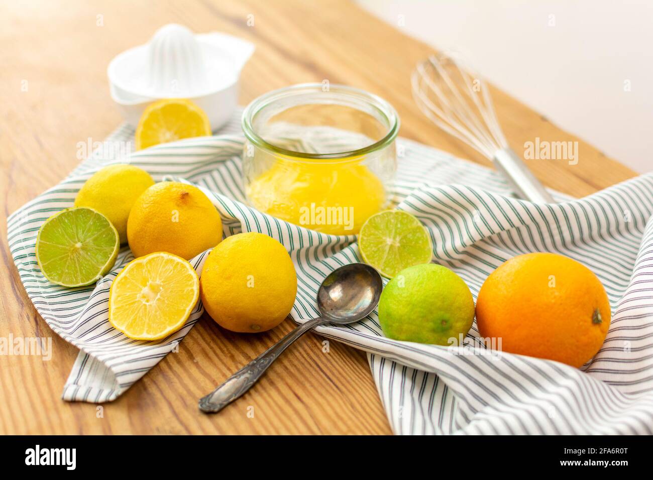 Eine Menge Zitrusfrüchte wie Zitronen, Orangen und Limetten auf einem Holztisch bereit, für Saft oder zum Backen, ein Glas mit Zitronenquark gepresst werden. Stockfoto