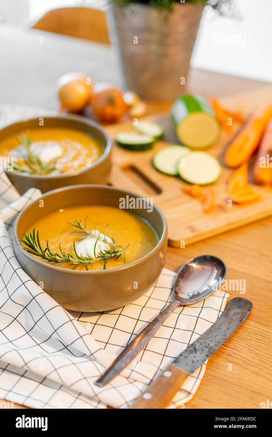 Eine schöne hausgemachte Mahlzeit mit einer frischen Gemüsesuppe mit Karotten und Zucchini und Zwiebeln, serviert auf einem alten Holztisch mit viel Garnierung. Stockfoto