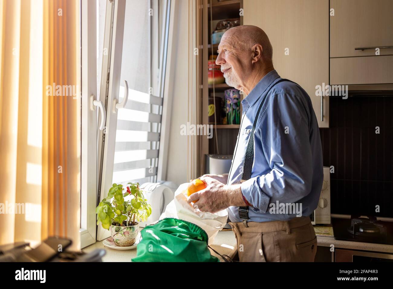 Älterer Mann, der zu Hause durch das Fenster schaut Stockfoto