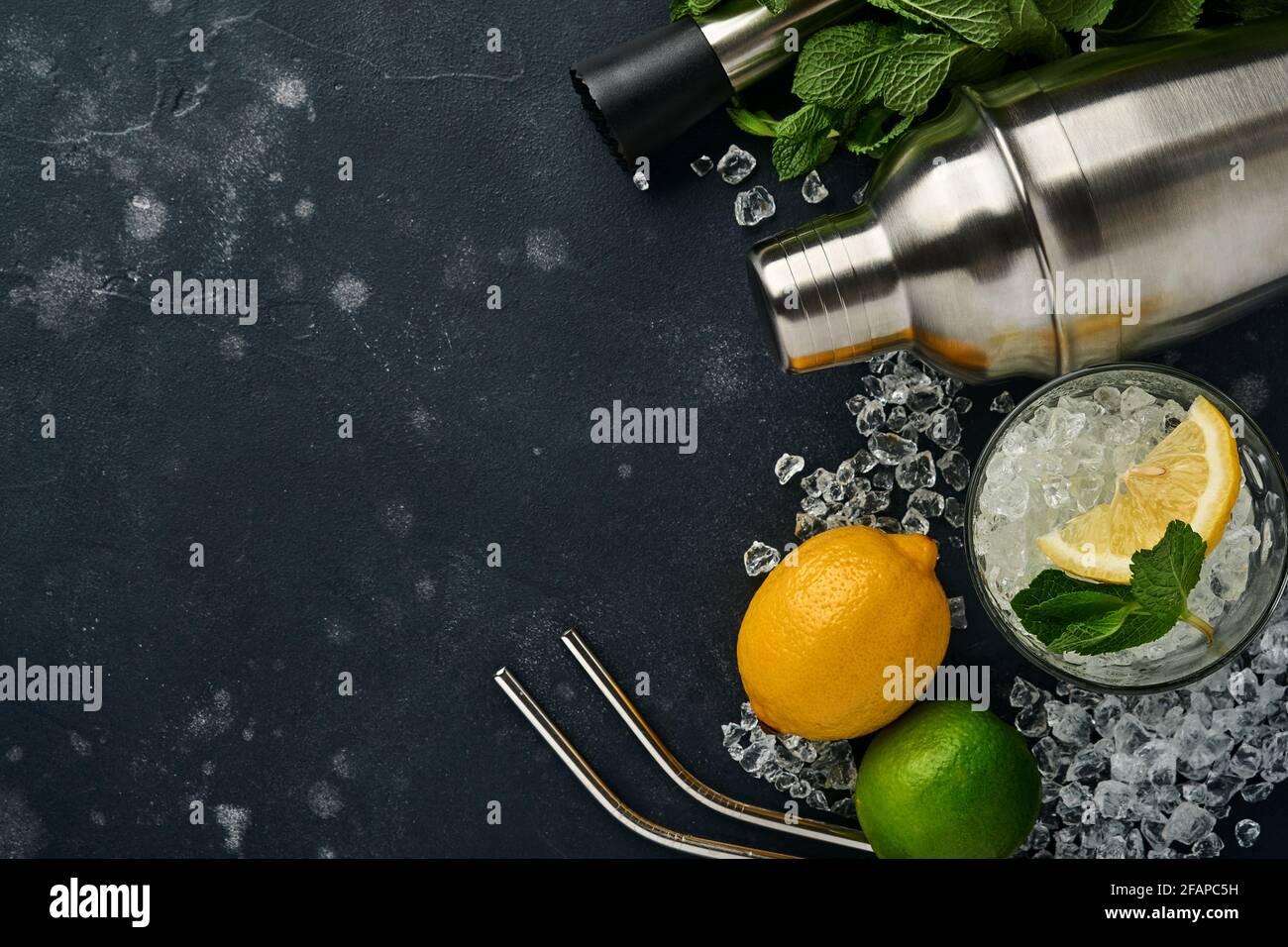 Mojito oder Lemonade Cocktail im Longdrinkglas mit Eiswürfeln, Minze und Limette auf schwarzem Steingrund mit Shaker und Becher. Menüleiste. Platz für Text Stockfoto