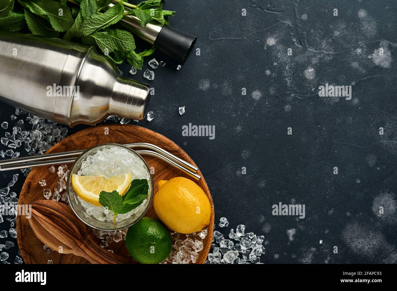 Mojito oder Lemonade Cocktail im Longdrinkglas mit Eiswürfeln, Minze und Limette auf schwarzem Steingrund mit Shaker und Becher. Menüleiste. Platz für Text Stockfoto