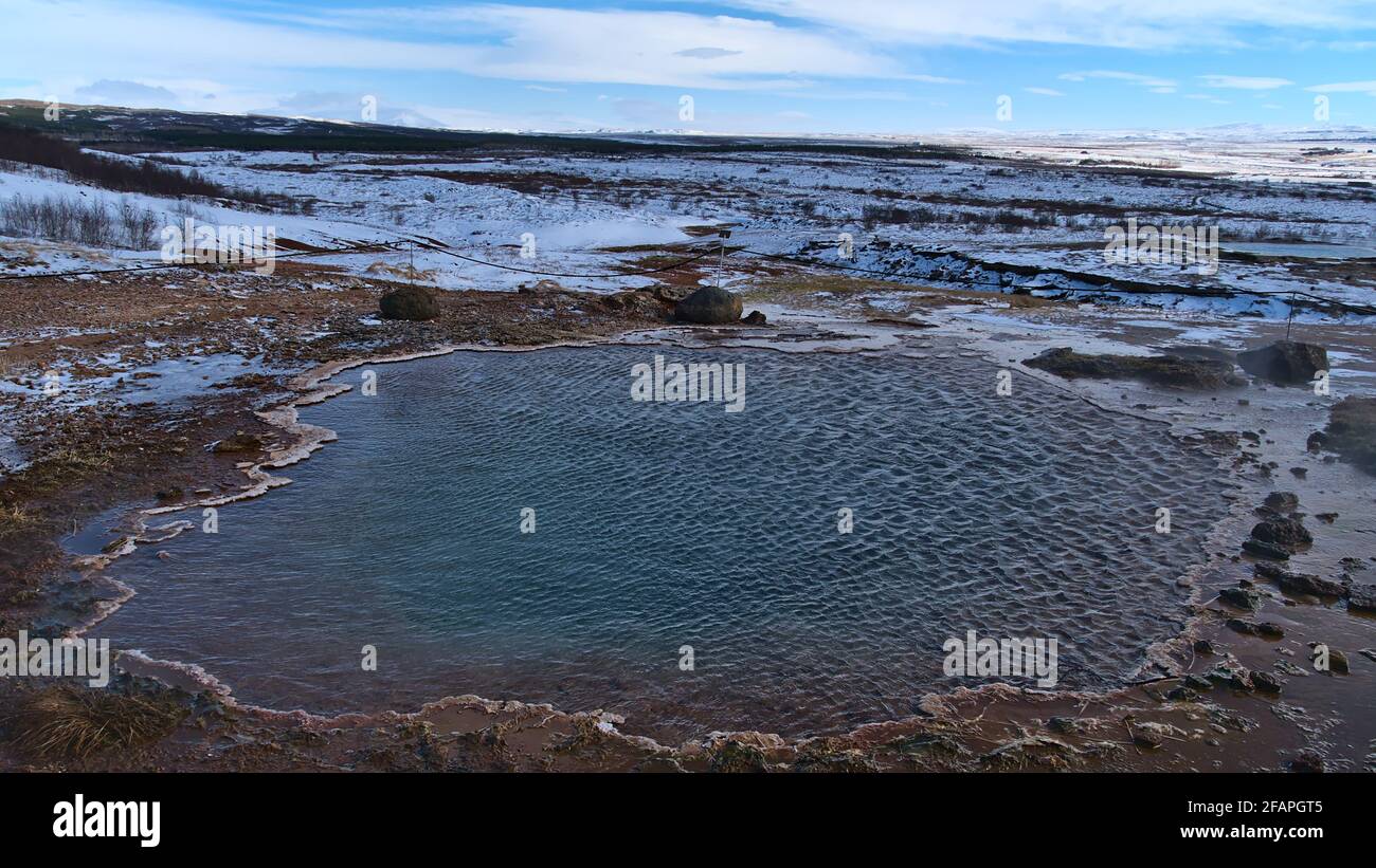 Heiße Quelle mit dampfendem Wasserbecken in Geysir im geothermischen Gebiet Haukadalur, Teil des Goldenen Kreises, Island in der Wintersaison an sonnigen Tag mit Schnee. Stockfoto