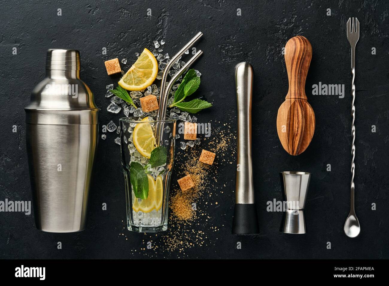 Mojito oder Lemonade Cocktail im Longdrinkglas mit Eiswürfeln, Minze und Limette auf schwarzem Steingrund mit Shaker und Becher. Menüleiste. Platz für Text Stockfoto