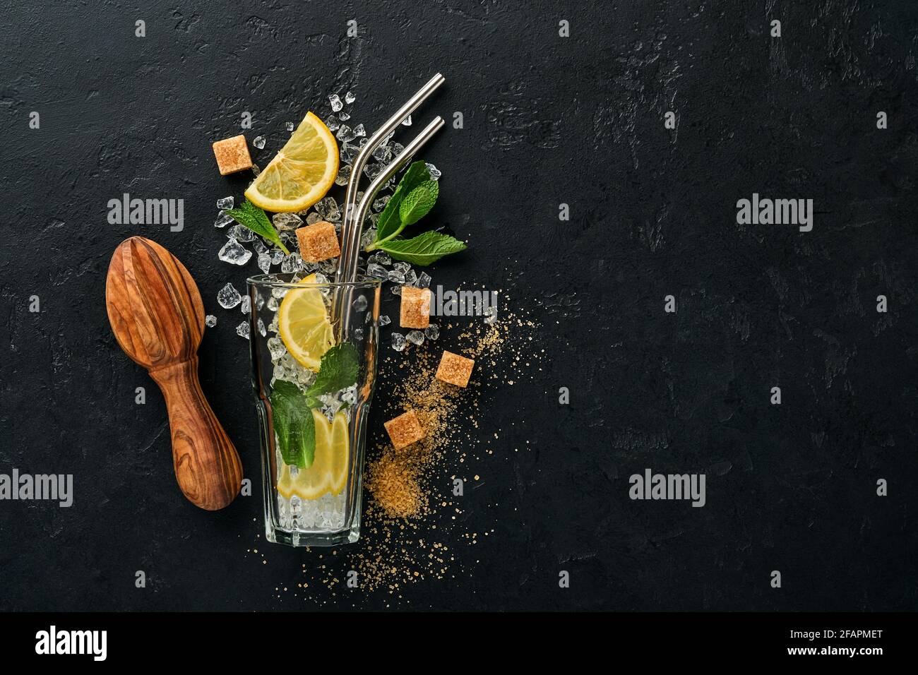 Mojito oder Lemonade Cocktail im Longdrinkglas mit Eiswürfeln, Minze und Limette auf schwarzem Steingrund mit Shaker und Becher. Menüleiste. Platz für Text Stockfoto