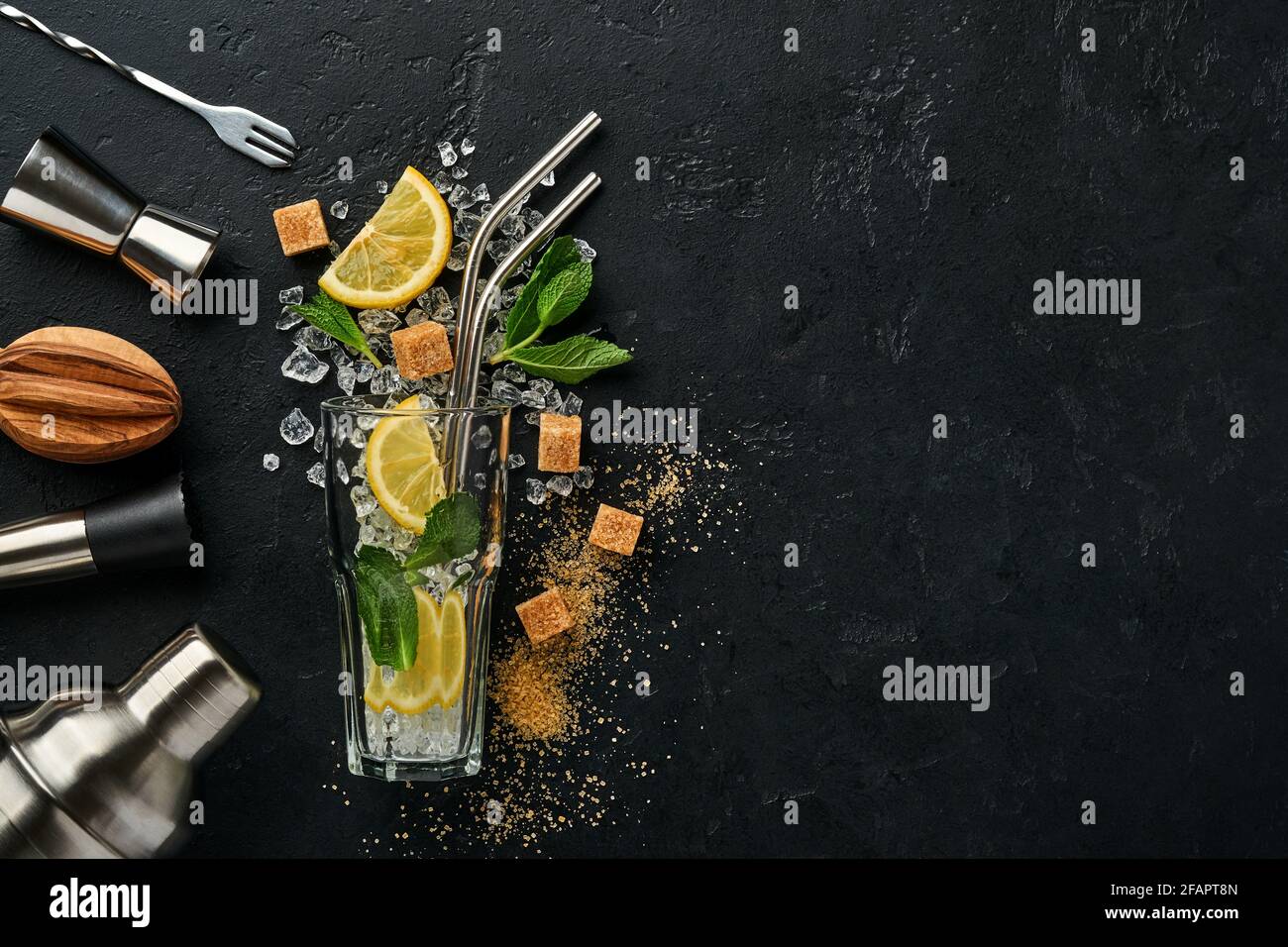 Mojito oder Lemonade Cocktail im Longdrinkglas mit Eiswürfeln, Minze und Limette auf schwarzem Steingrund mit Shaker und Becher. Menüleiste. Platz für Text Stockfoto