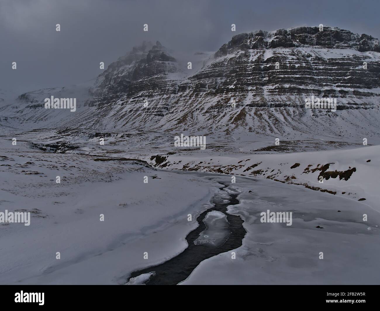 Zerklüftete Landschaft mit gefrorenem Fluss und rauhen, schneebedeckten Bergen mit steilen Hängen in der Nähe von Grundarfjörður auf der Halbinsel Snæfellsnes im Westen Islands. Stockfoto