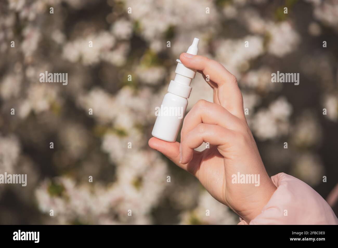 Allergiekonzept, junge Frau mit Nase oder Nasenspray in der Hand vor einem blühenden Baum während der Frühjahrssaison, Gesundheitsversorgung Stockfoto