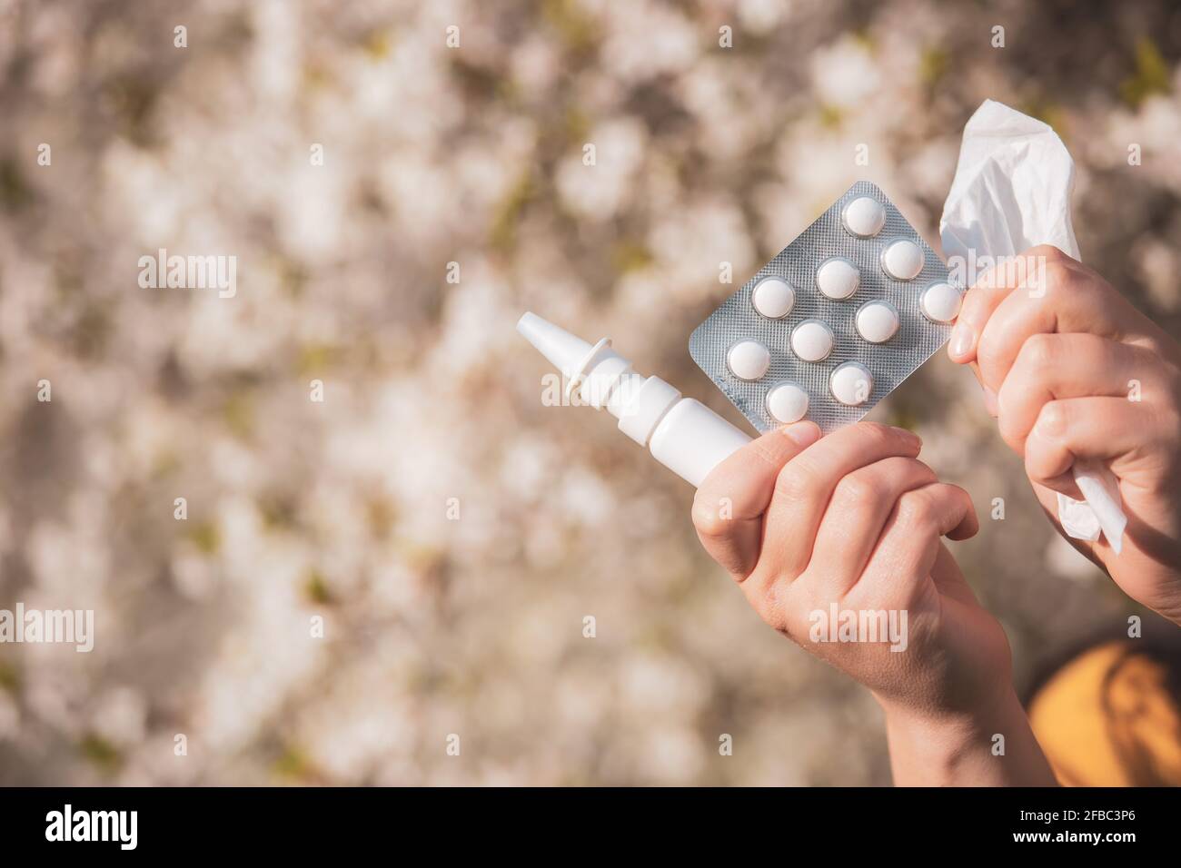 Allergiekonzept, junge Frau mit Pillen oder Medikamenten und Nase oder Nasenspray gegen die starke Allergie in der Hand vor blühenden Bäumen im Frühjahr Stockfoto