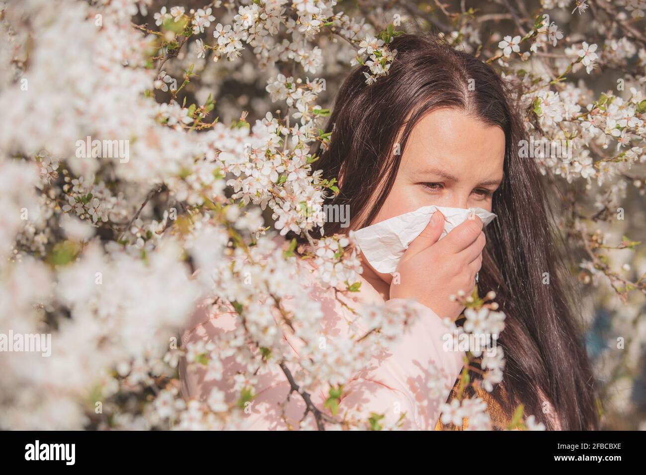 Konzept der Frühjahrsallergie-Symptome, junge Frau niest vor dem Blühen eines Baumes, Allergie gegen Pollen und Blütezeit, Gesundheitsversorgung Stockfoto