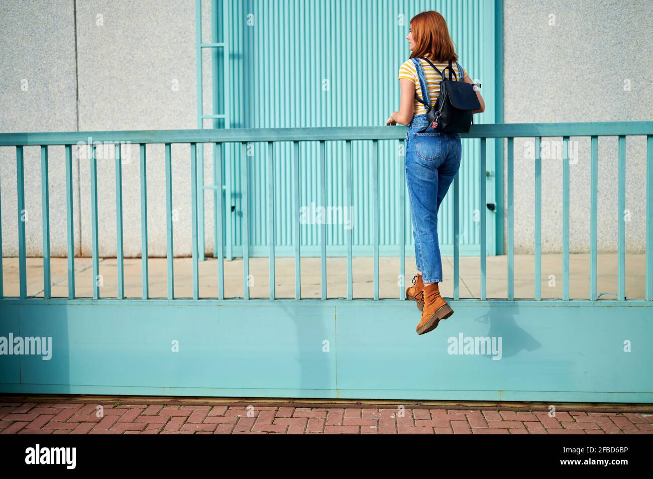 Junge Frau klettert auf türkisblauem Geländer Stockfoto