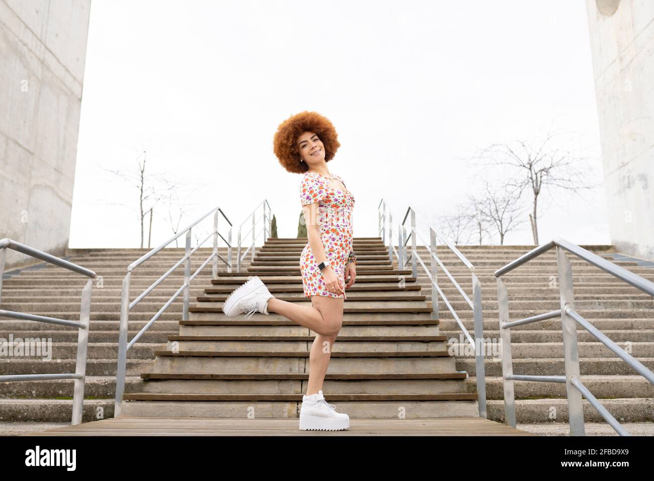 Junge Frau, die am Geländer auf einem Bein steht Stockfoto