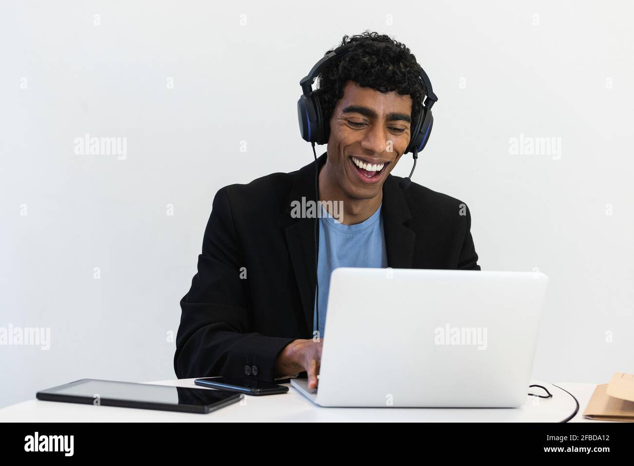 Fröhlicher Geschäftsmann mit Headset, der an einem Videoanruf über einen Laptop teilnimmt Büro Stockfoto