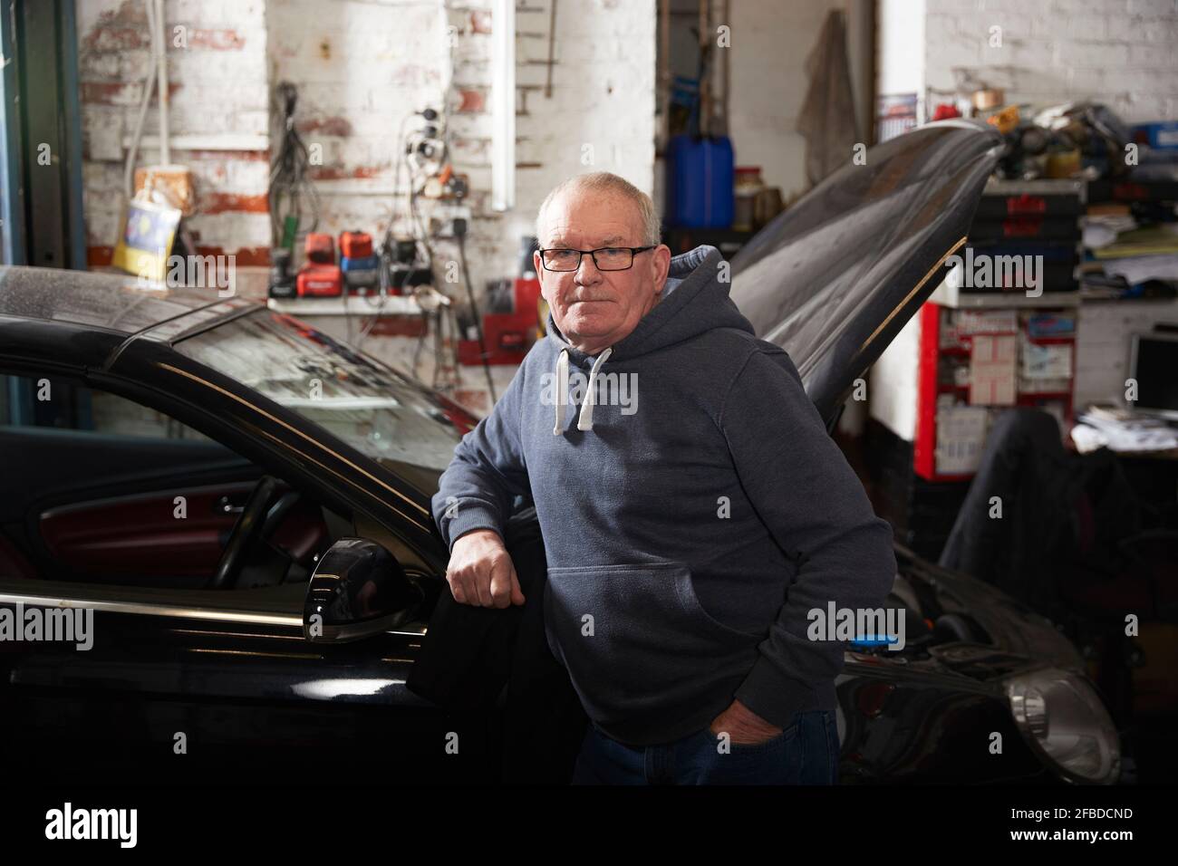 Selbstbewusster männlicher Mechaniker mit der Hand in der Tasche, die sich auf das Auto stützt In der Werkstatt Stockfoto