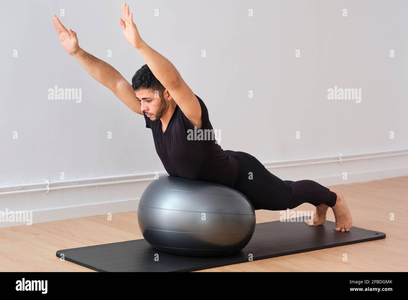 Mann, der im Fitnessraum Pilates auf dem Fitnessball trainiert Stockfoto