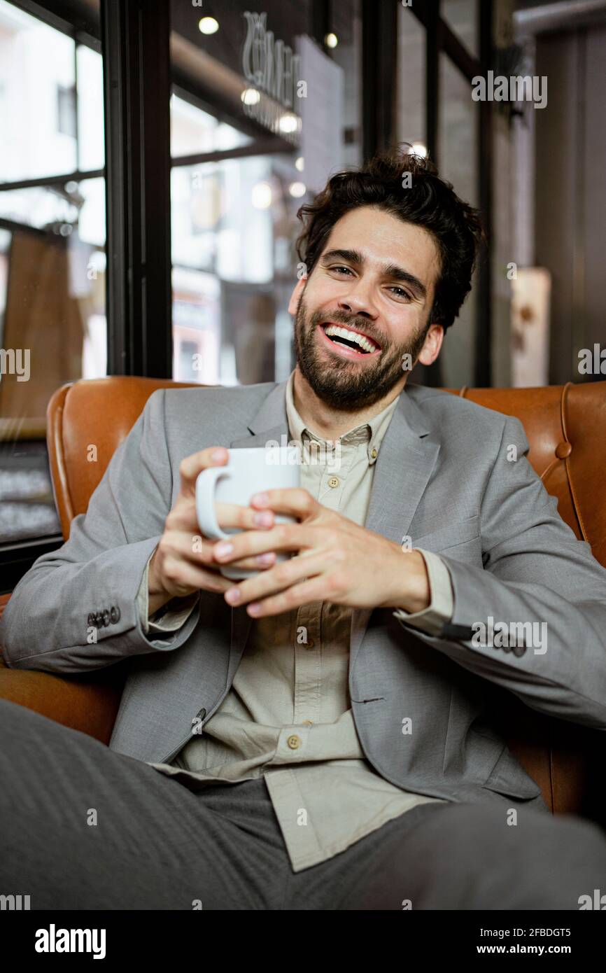 Ein fröhlicher Geschäftsmann hält eine Kaffeetasse in der Hand, während er im Café sitzt Stockfoto