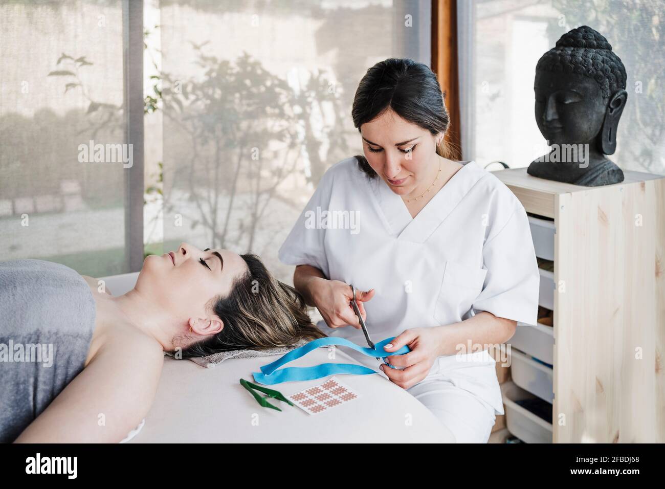 Weibliche Physiotherapeutin schneidet elastisches therapeutisches Klebeband am Tisch ein Klinik Stockfoto