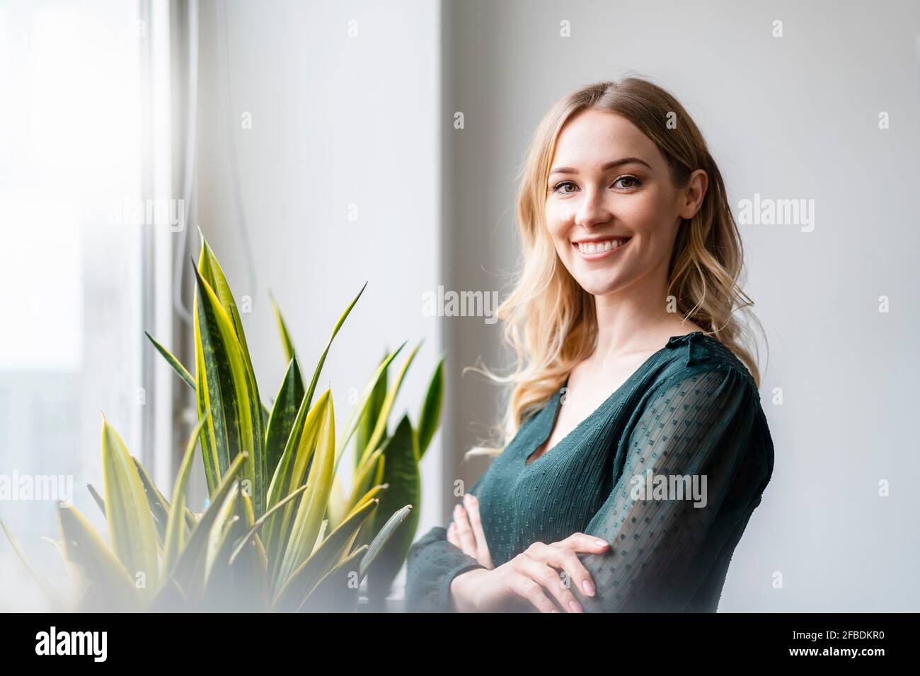 Lächelnde Geschäftsfrau mit gekreuzten Armen, die im Büro stehen Stockfoto