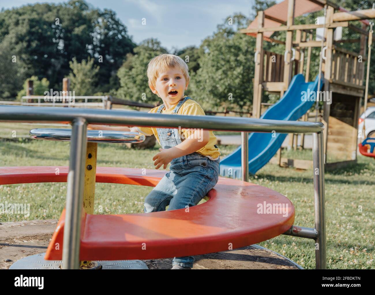 Charmanter Junge sitzt auf fröhlichen gehen rund auf dem Spielplatz Stockfoto