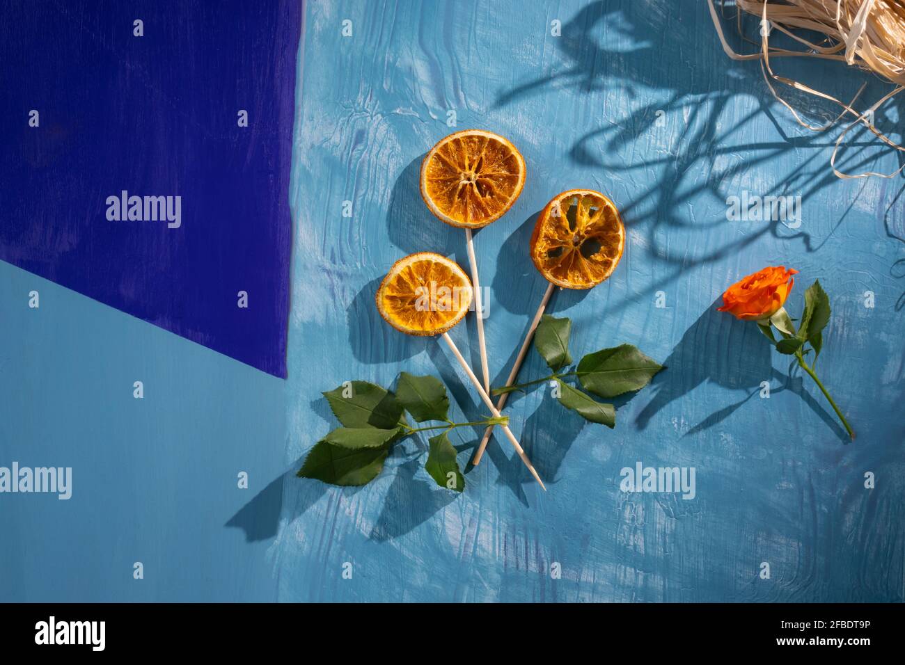 Blume aus getrockneten orangefarbenen Scheiben auf blauem Holzhintergrund mit schönen Schatten und Kopierraum, Grußkartenkonzept Stockfoto