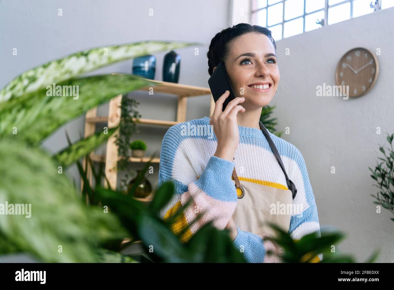 Lächelnde Gärtnerin im Gespräch auf dem Smartphone in der Werkstatt Stockfoto