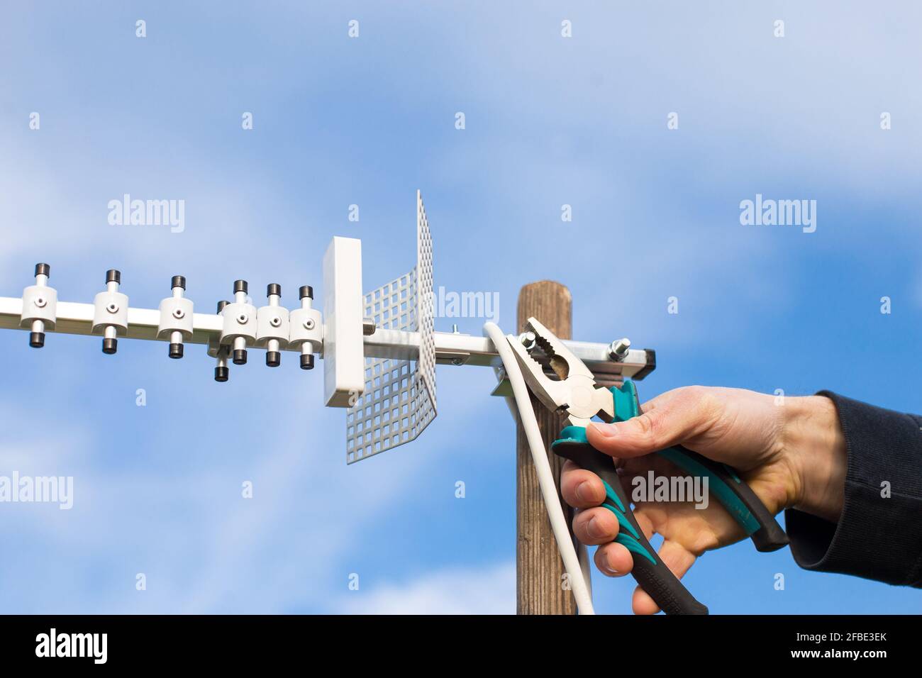 Männliche Hände installieren 4G-Antenne direktional Typ mit Zange, Nahaufnahme auf blauem Hintergrund. Stockfoto