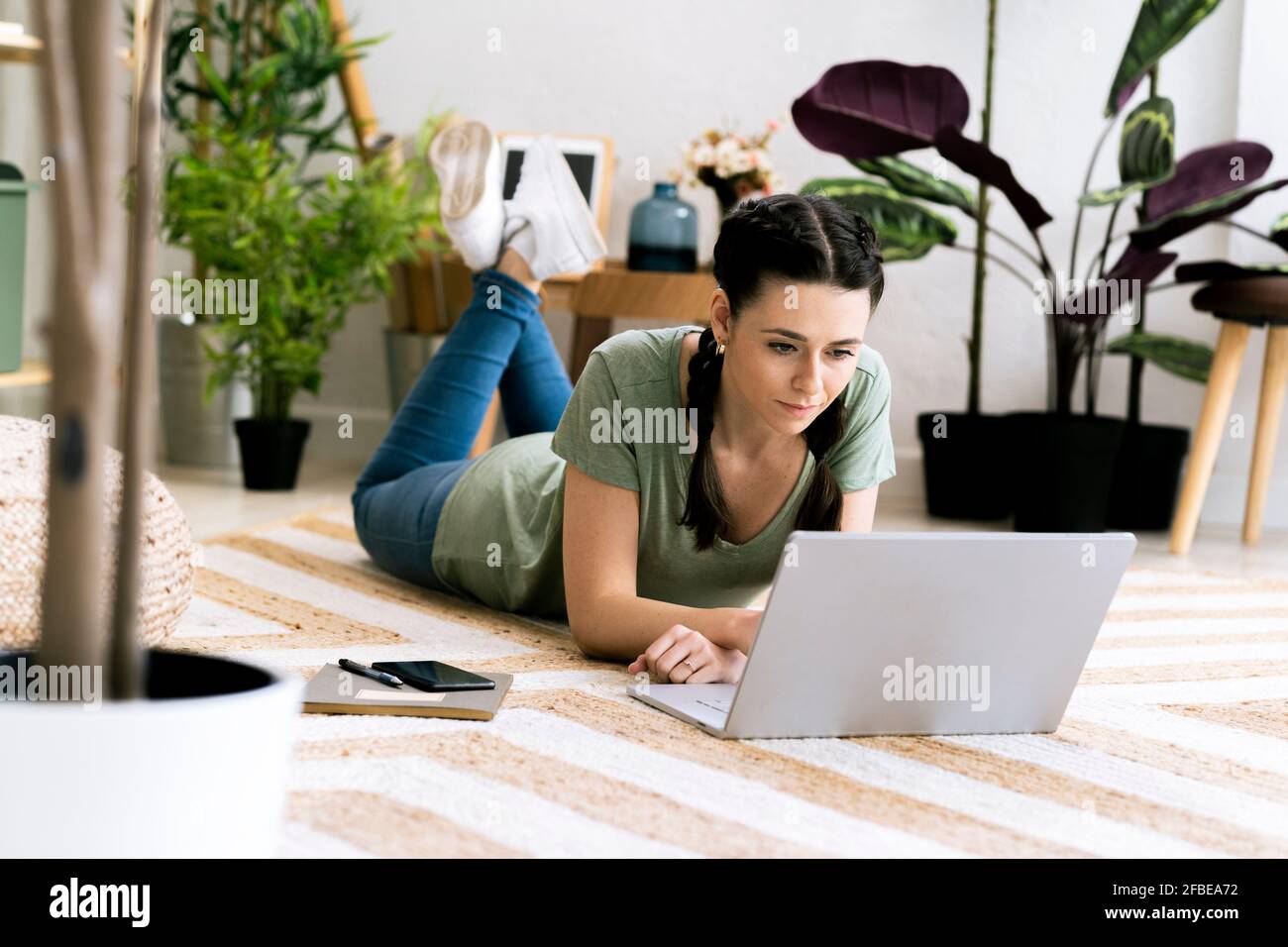Schöne Frau mit Laptop, während sie zu Hause auf dem Teppich lag Stockfoto