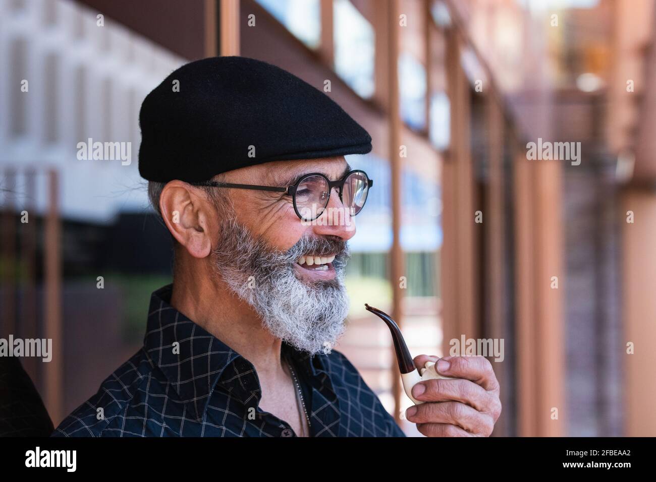 Glücklicher reifer Mann, der rauchendes Rohr hält, während er wegschaut Stockfoto