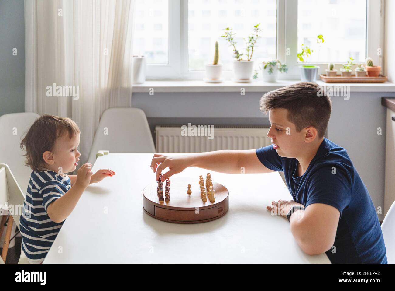 Junge spielt Schach mit jüngeren Geschwisterkinder auf dem Tisch zu Hause Stockfoto