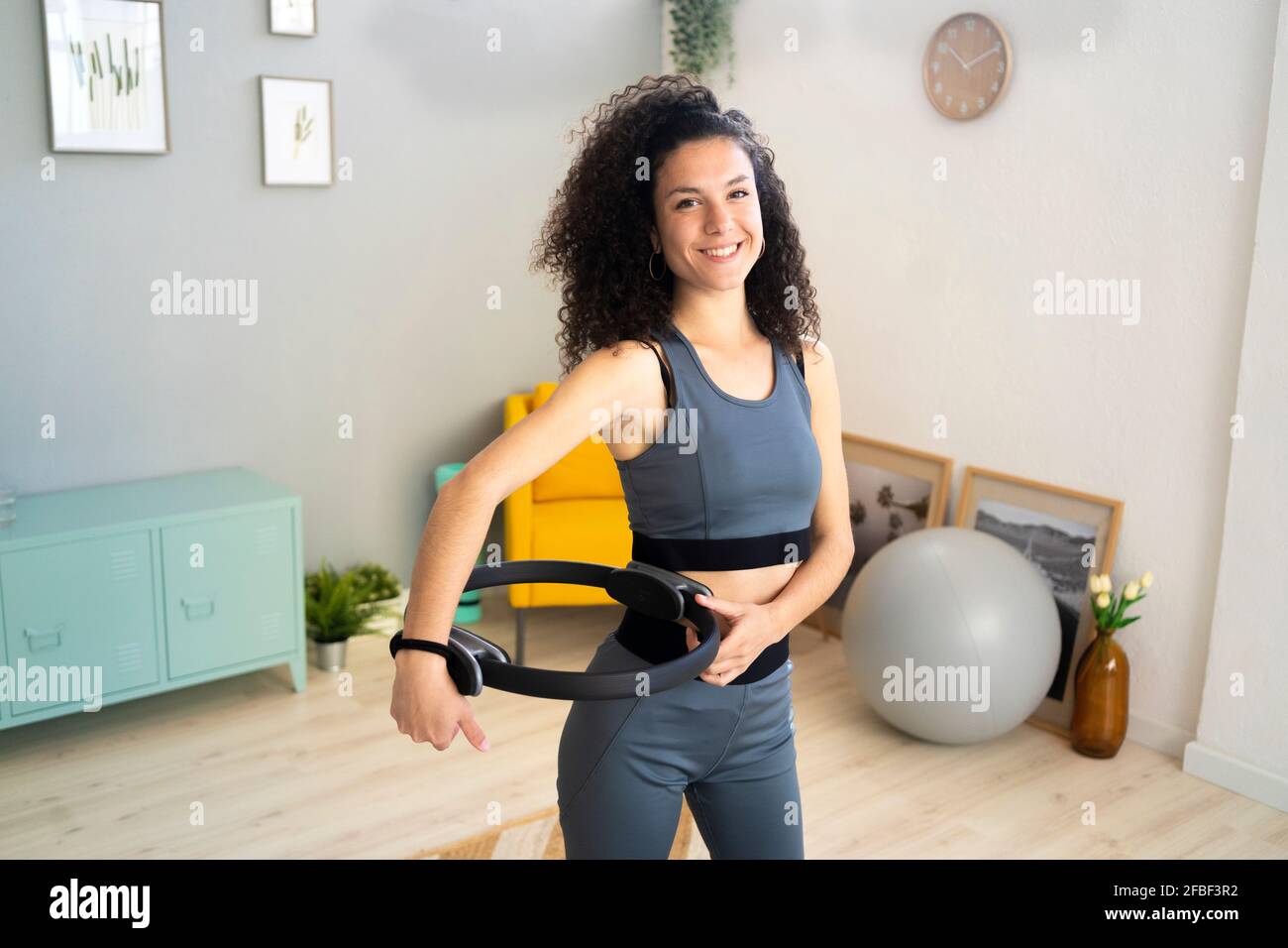 Lächelnde Frau mit Pilates-Ring zu Hause stehend Stockfoto