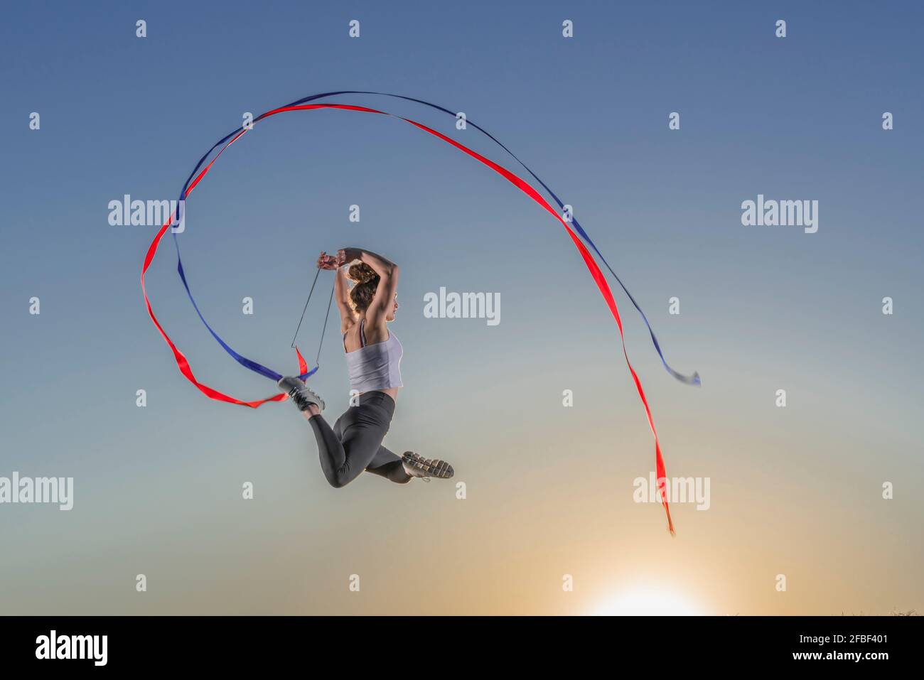 Weibliche Turnerin, die während des Sonnenuntergangs mit Bändern springt Stockfoto
