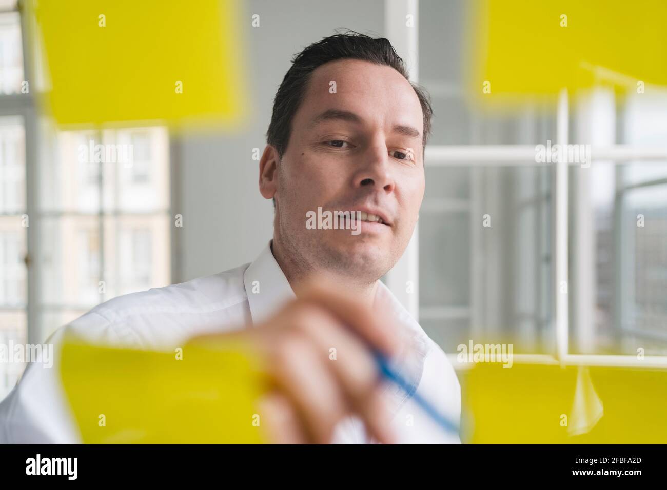 Businessman Brainstorming mit Notizen auf transparentem Wipe Board am Arbeitsplatz Stockfoto