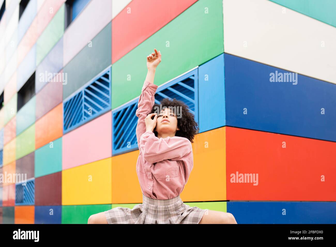 Tänzerin mit erhobener Hand vor einem farbenfrohen Gebäude Stockfoto