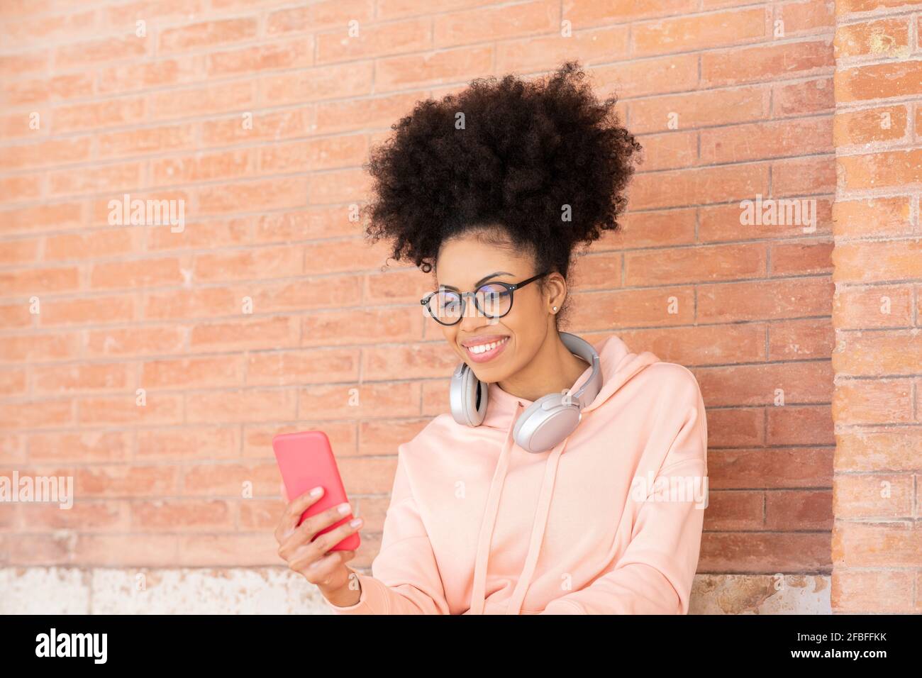 Afro-Frau mit Smartphone an der roten Ziegelwand Stockfoto