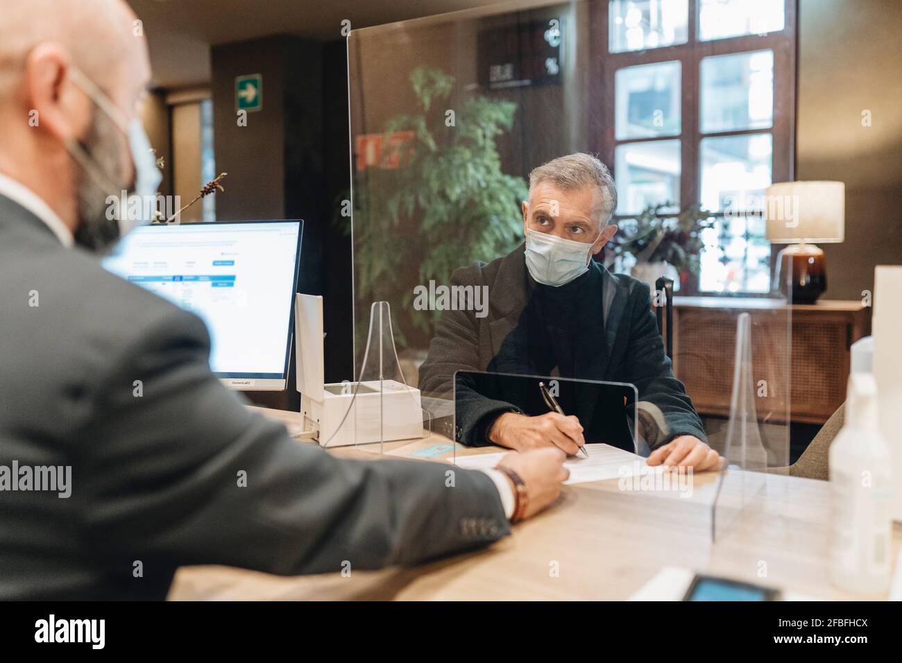 Mann, der an der Hotelrezeption ein Formular mit einer Gesichtsmaske trägt Stockfoto