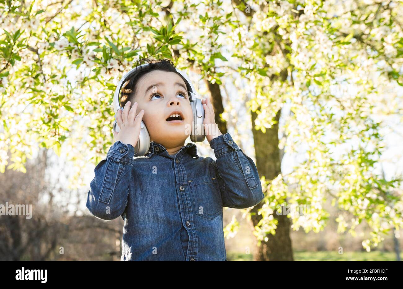 Überraschte Jungen, die aufschauten, während sie über kabellose Kopfhörer Musik hörten Im Park Stockfoto