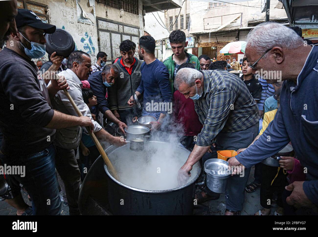 Gaza, Palästina. April 2021. Der Palästinenser Walid Al-Hattab (trägt ein kariertes Hemd) verteilt während des heiligen Monats Ramadan im Stadtteil Shejaiya von Gaza City kostenloses Essen an arme Familien. Kredit: SOPA Images Limited/Alamy Live Nachrichten Stockfoto