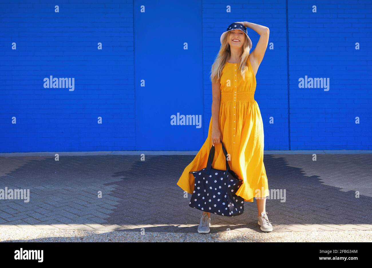 Lächelnde Frau mit Seesasche, die an sonnigen Tagen vor der blauen Wand steht Stockfoto