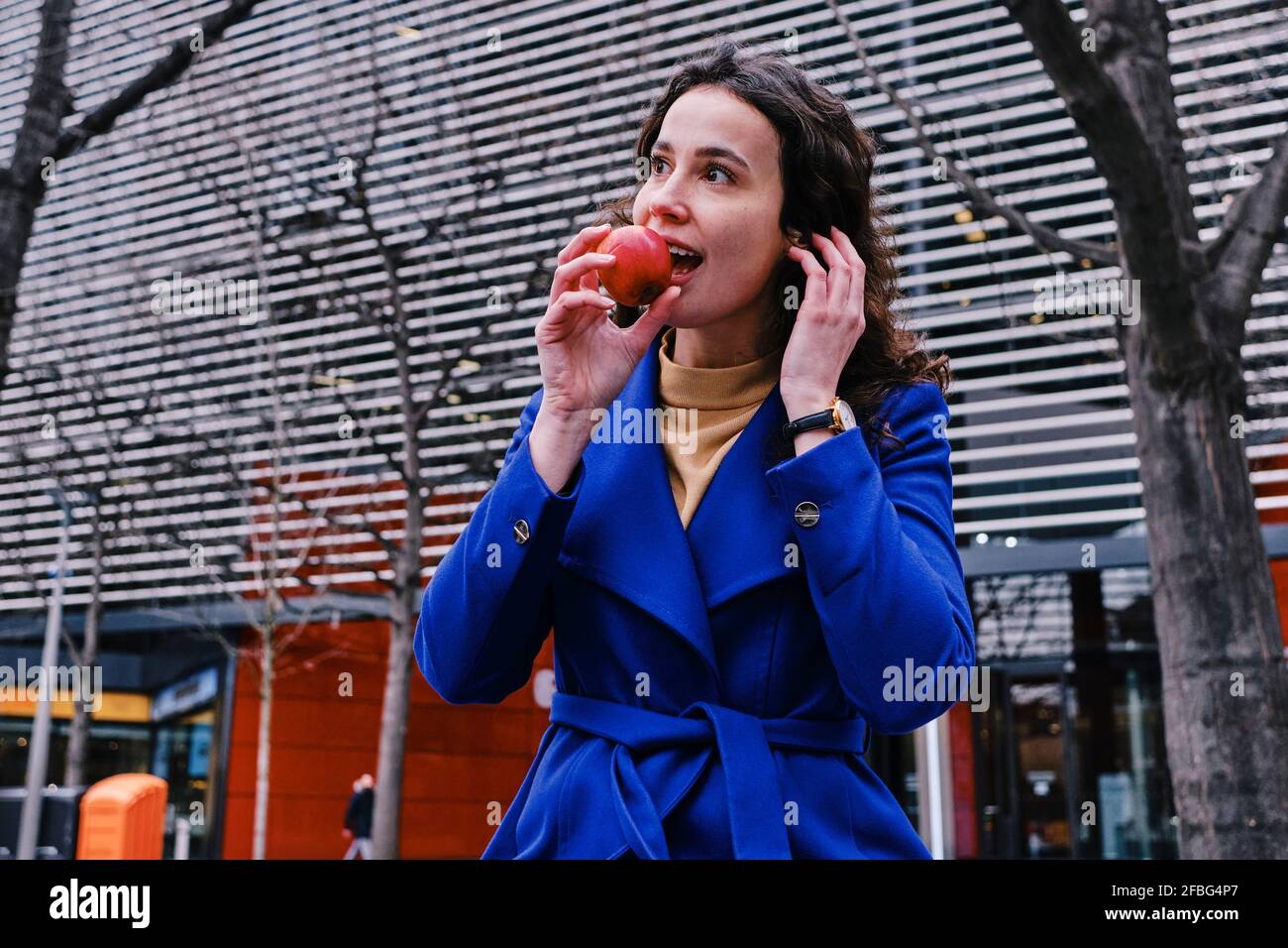 Geschäftsfrau im Trenchcoat, die Apfel isst Stockfoto