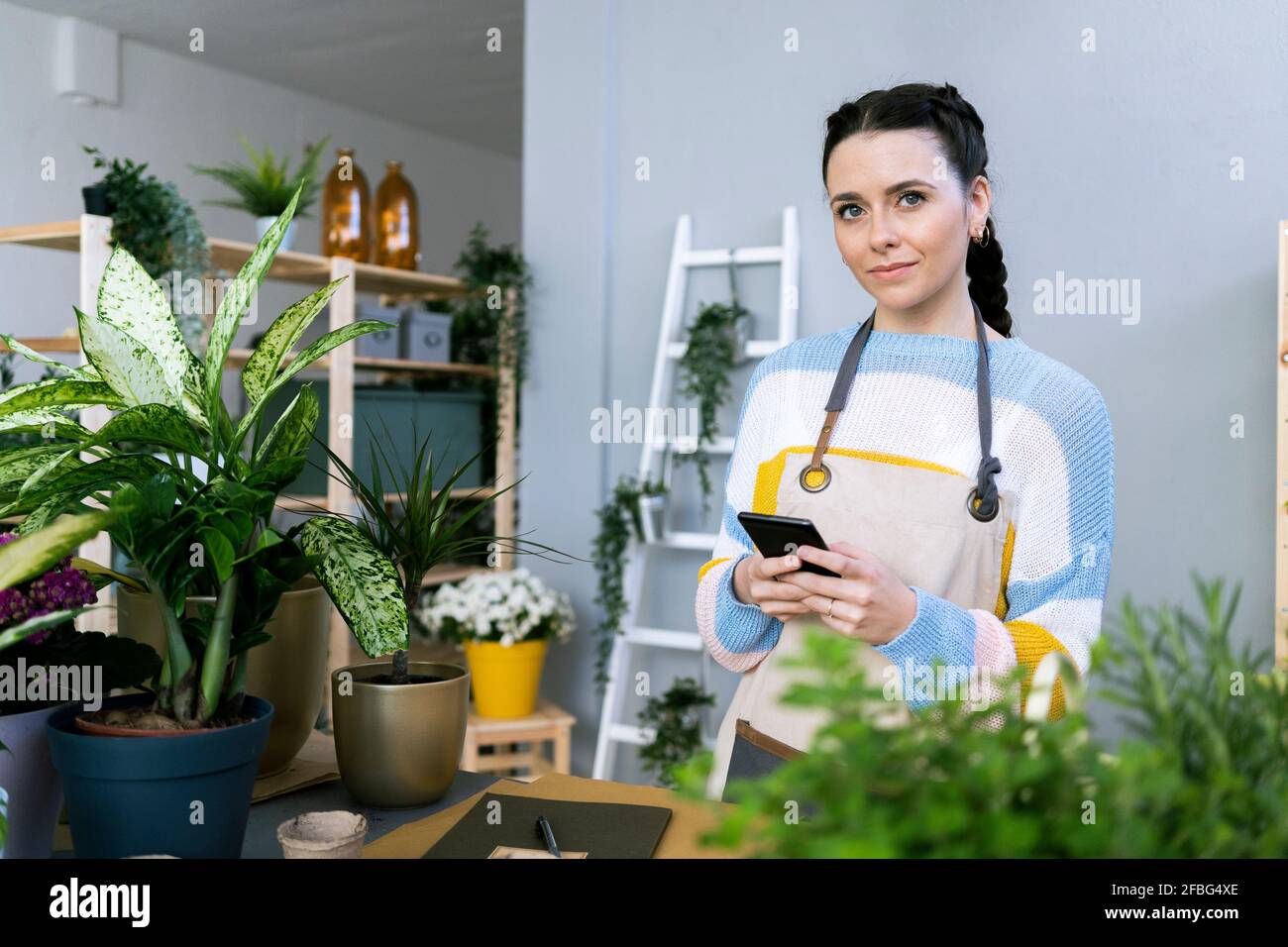 Schöne Gärtnerin, die wegschaut, während sie das Smartphone anhält Workshop Stockfoto