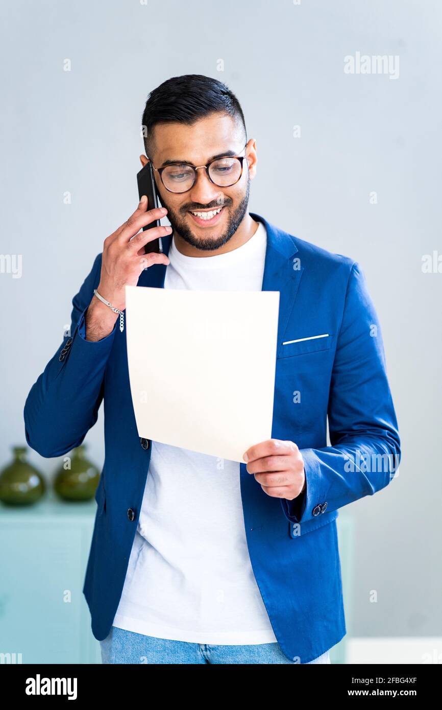 Fröhlicher Geschäftsmann, der Papier hält, während er mit dem Smartphone spricht Büro Stockfoto
