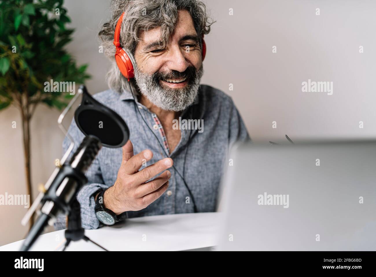 Lächelndes, männliches Podcasting, während man Kopfhörer im Büro trägt Stockfoto