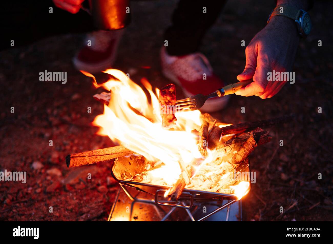 Mann, der Fleisch über dem Holzofen röstet, während er bei zelte Nacht Stockfoto