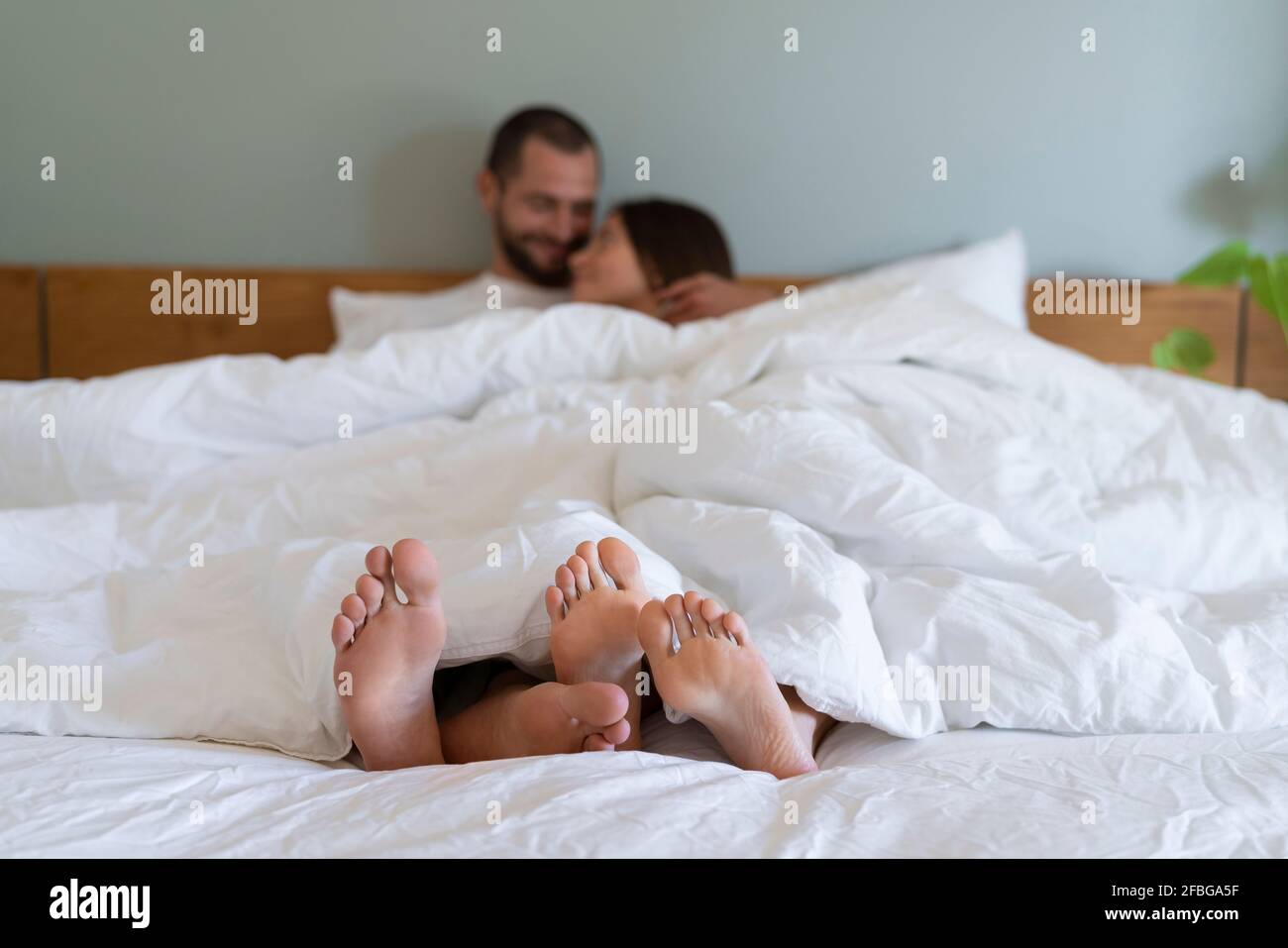 Glückliches Paar mit weißem Laken, das im Schlafzimmer auf dem Bett kuschelte Zu Hause Stockfoto