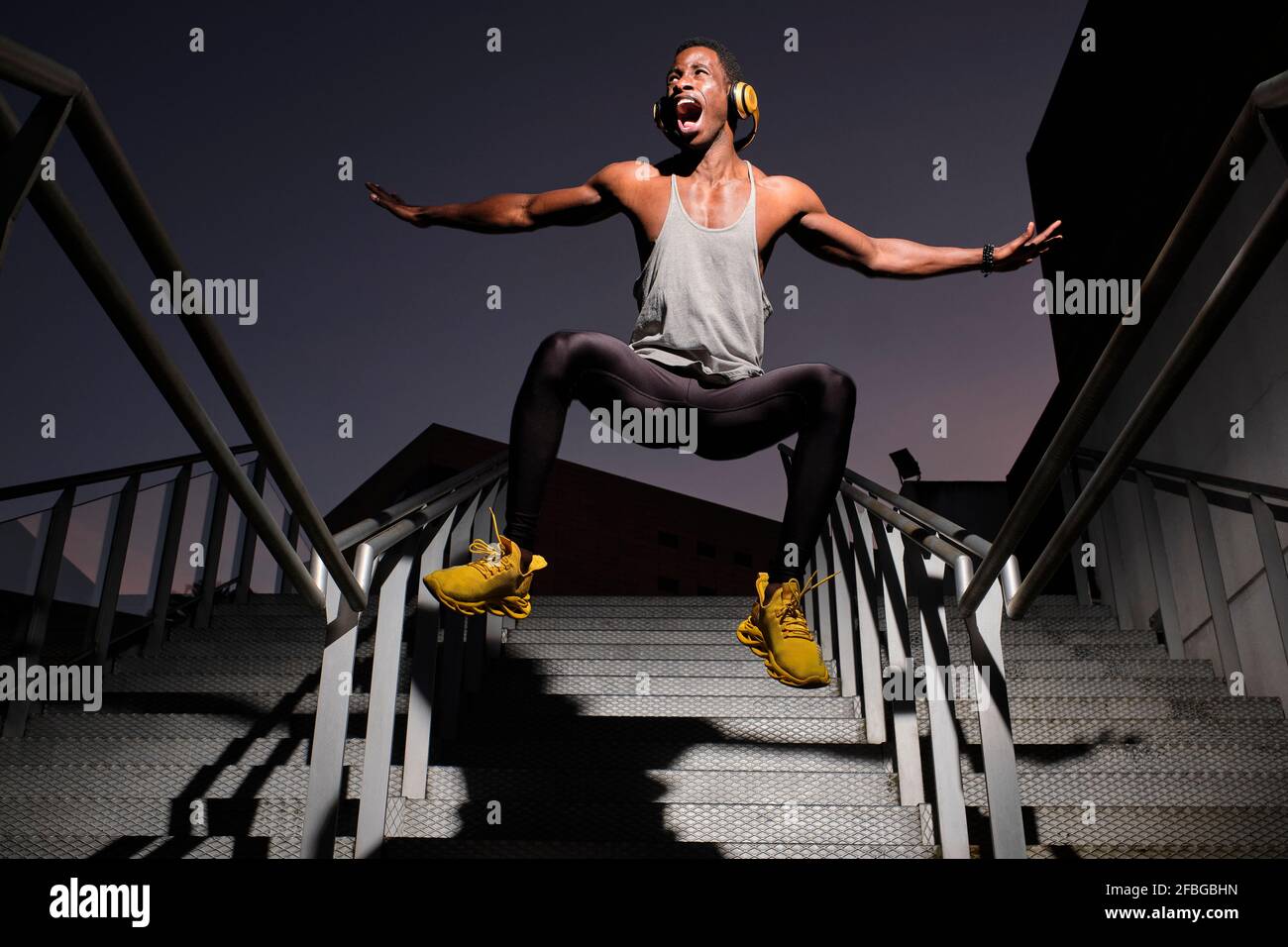 Verspielter junger Mann mit Kopfhörern, die von einer metallischen Treppe springen Stockfoto