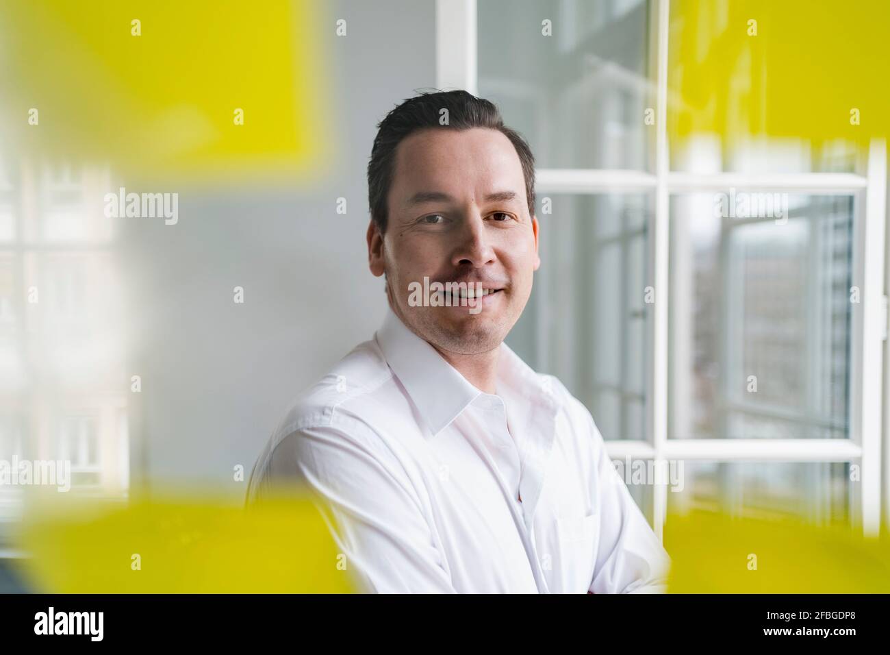 Lächelnder Geschäftsmann, der am Arbeitsplatz durch ein transparentes Wipe Board schaut Stockfoto