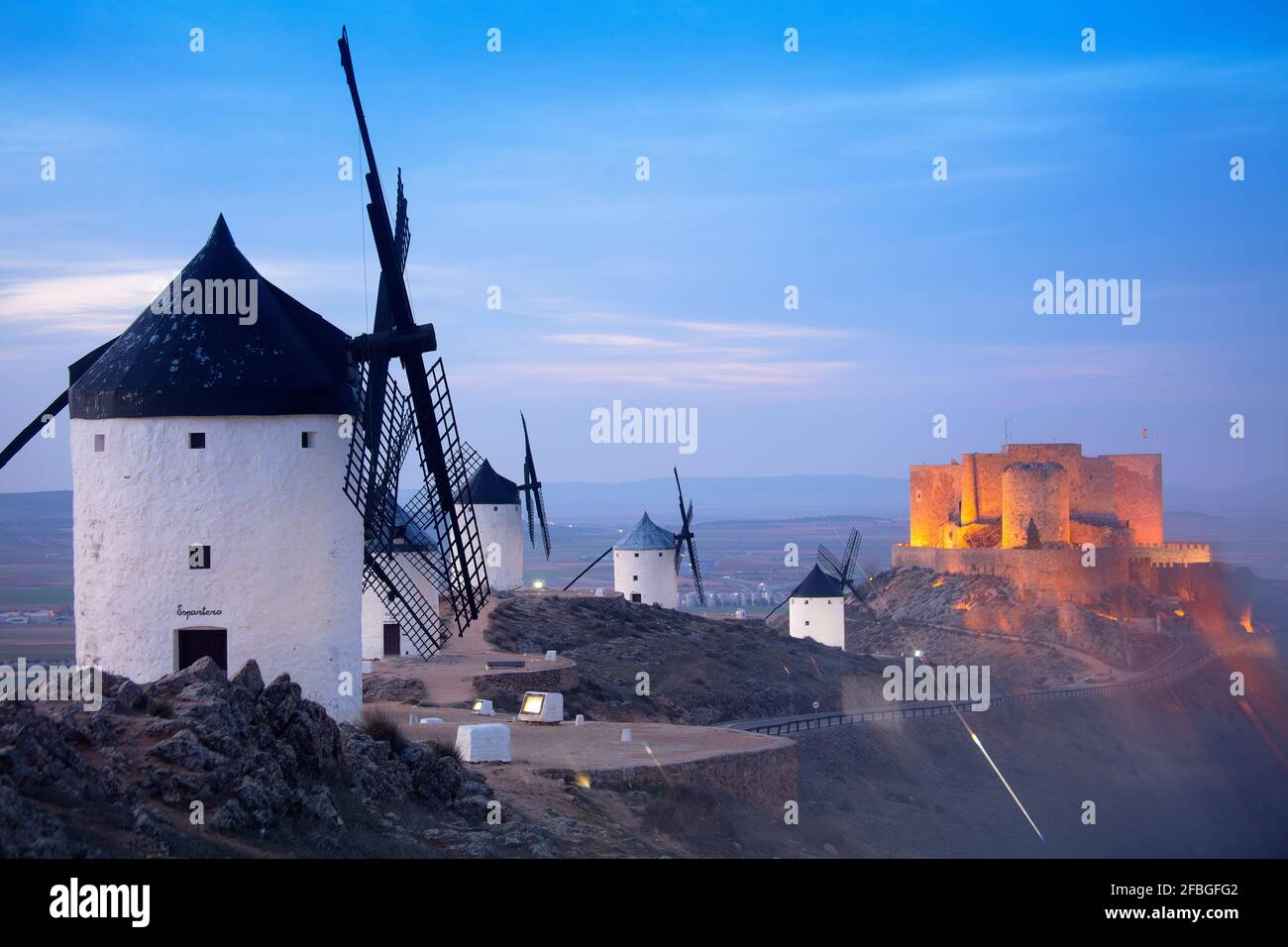 Spanien, Provinz Toledo, Consuegra, Historische Windmühlen in der Abenddämmerung mit Schloss La Muela im Hintergrund Stockfoto