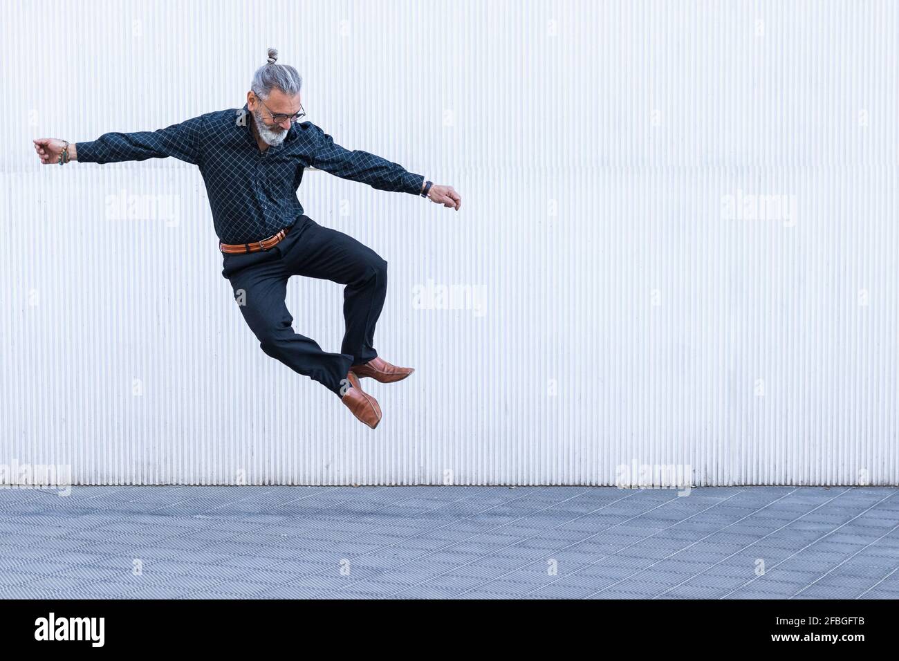 Reifer Mann schaut nach unten, während er auf dem Fußweg springt Stockfoto