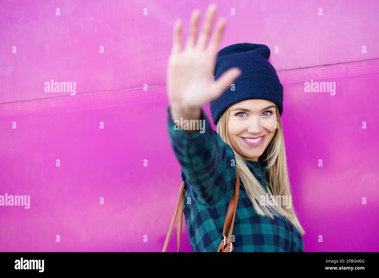 Lächelnde Frau mit Stop-Geste an der rosa Wand Stockfoto